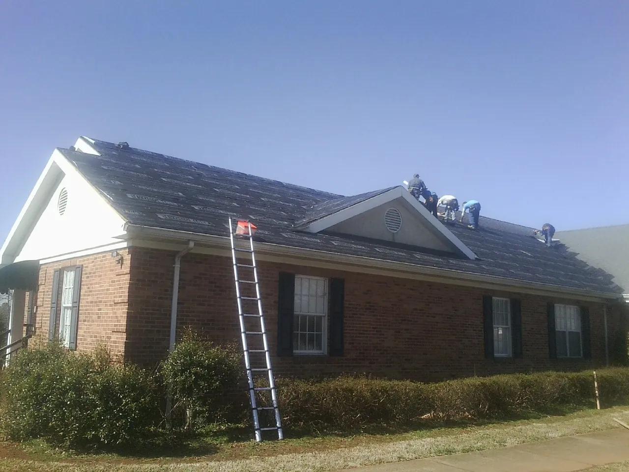 Crew tearing shingles off a brick ranch roof with a ladder set — Metal Roof Repair work by our crew in West Lafayette
