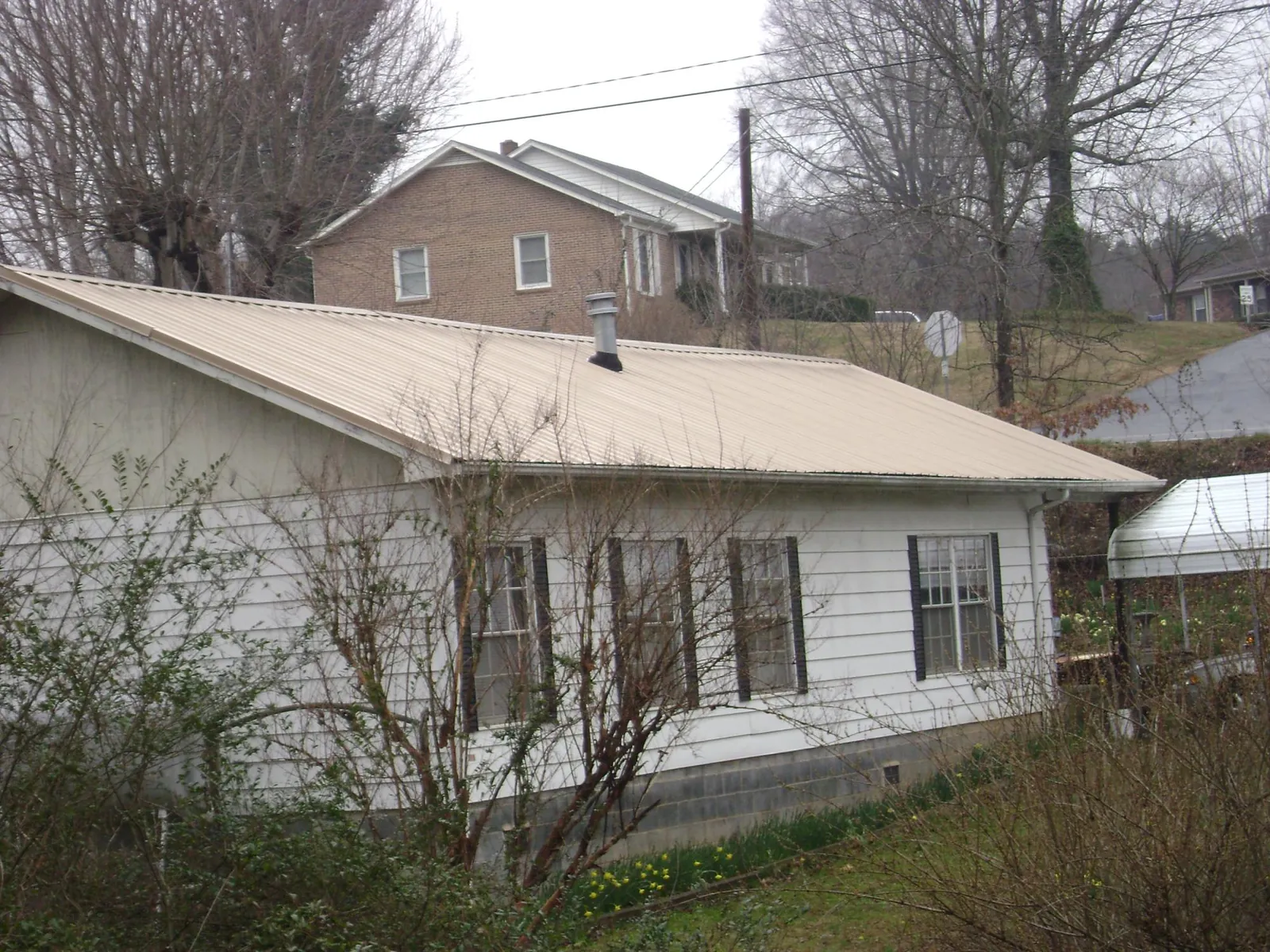 Tan metal roof on a white sided house set into a hillside — Commercial Roofing by Roofing Brothers in West Lafayette